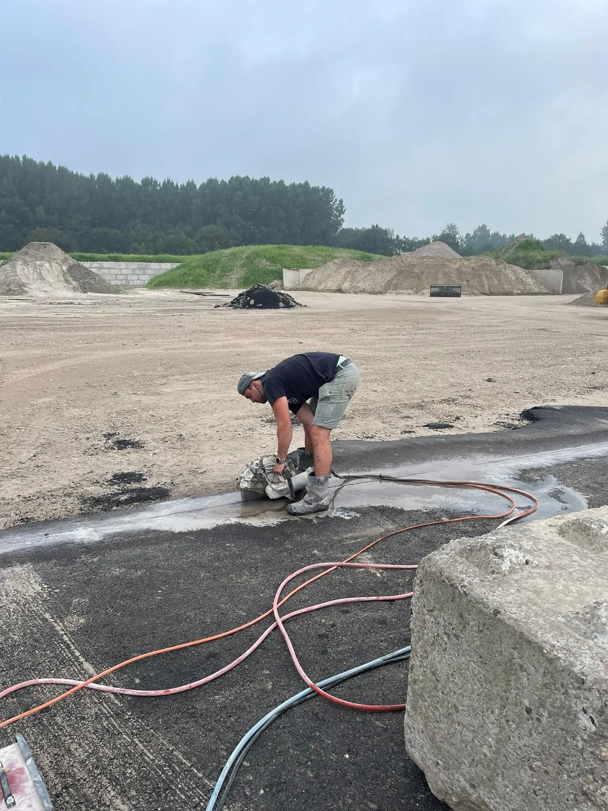 Medewerker maakt met een handzaag een zaagsnede in asfalt op een buitenterrein