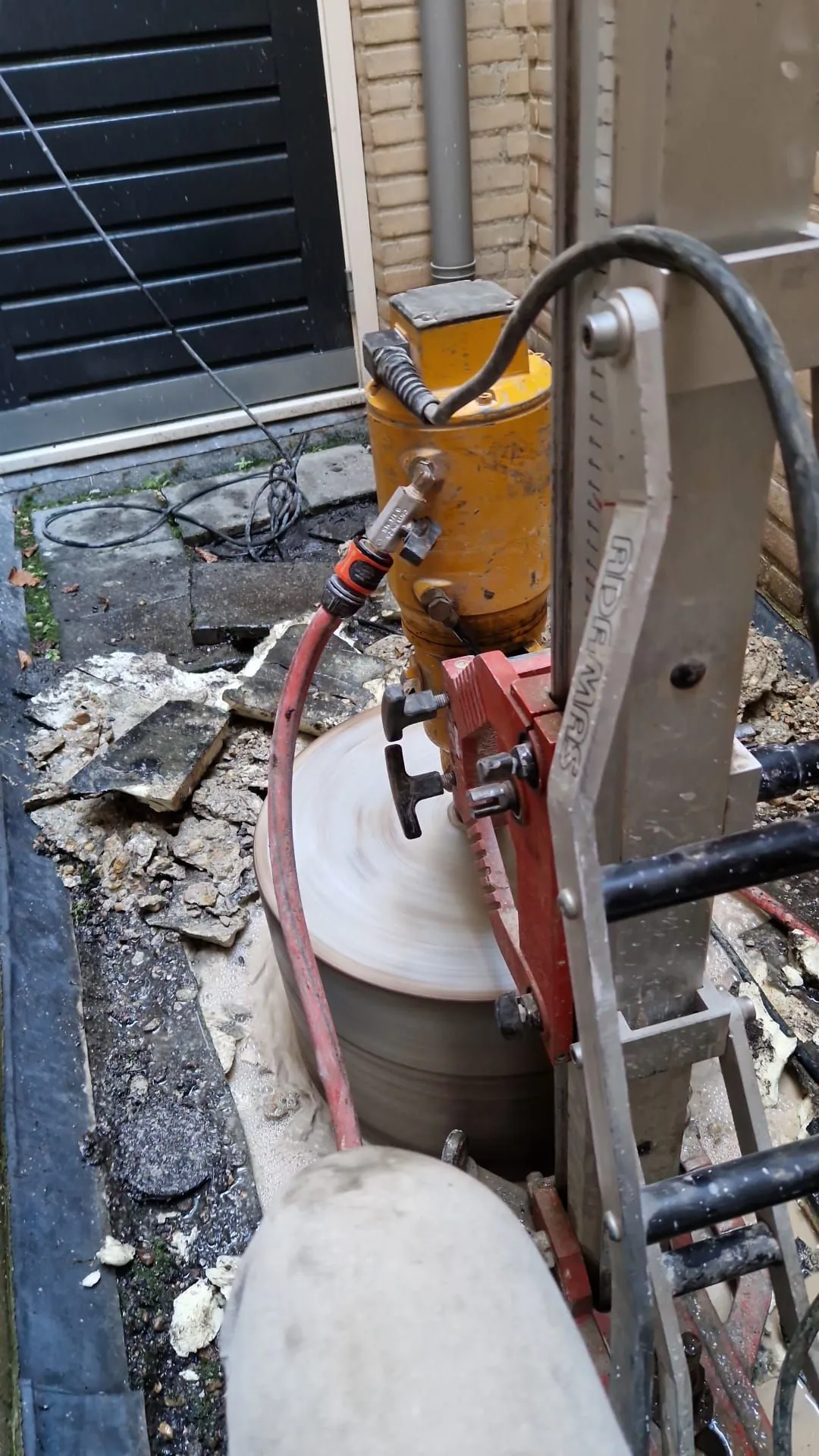 Diamantboor op statief maakt een verticale boring buiten naast een gevel